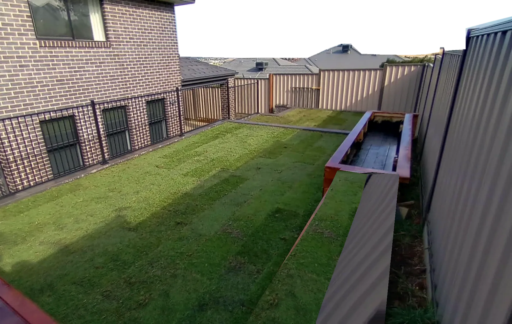 Fresh turf with a timber bench and planter box built by Rick's Landscaping, looking out to the hills