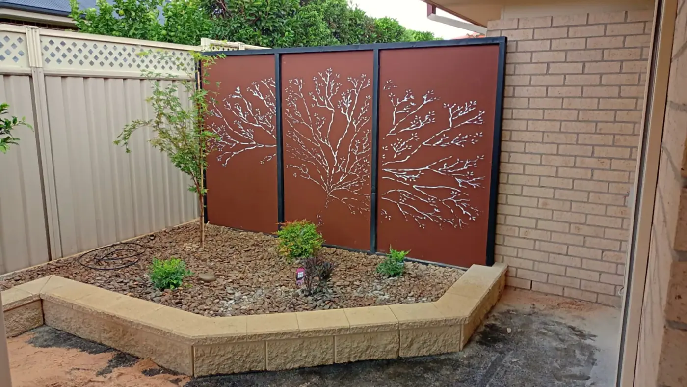 Three rust-coloured corten screens with a tree pattern behind a new block-edged garden bed