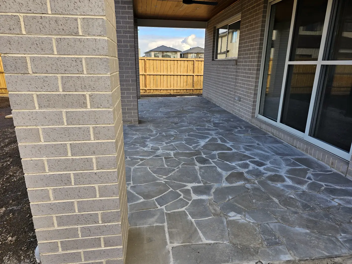 Grey crazy-paving flagstones laid under an alfresco beside a brick column