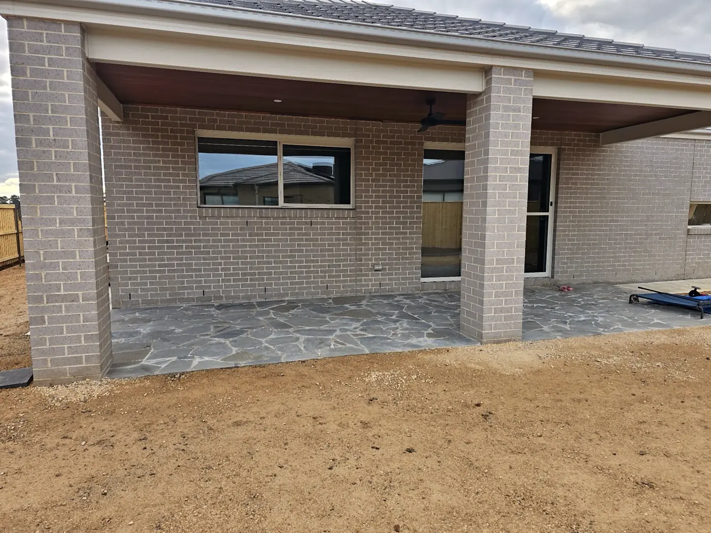 Wide view of a flagstone alfresco floor under the roofline of a brick home