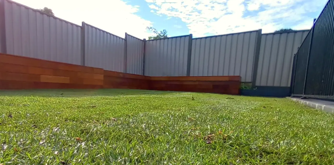 Wide view of a new lawn with timber sleeper edging along a grey Colorbond fence