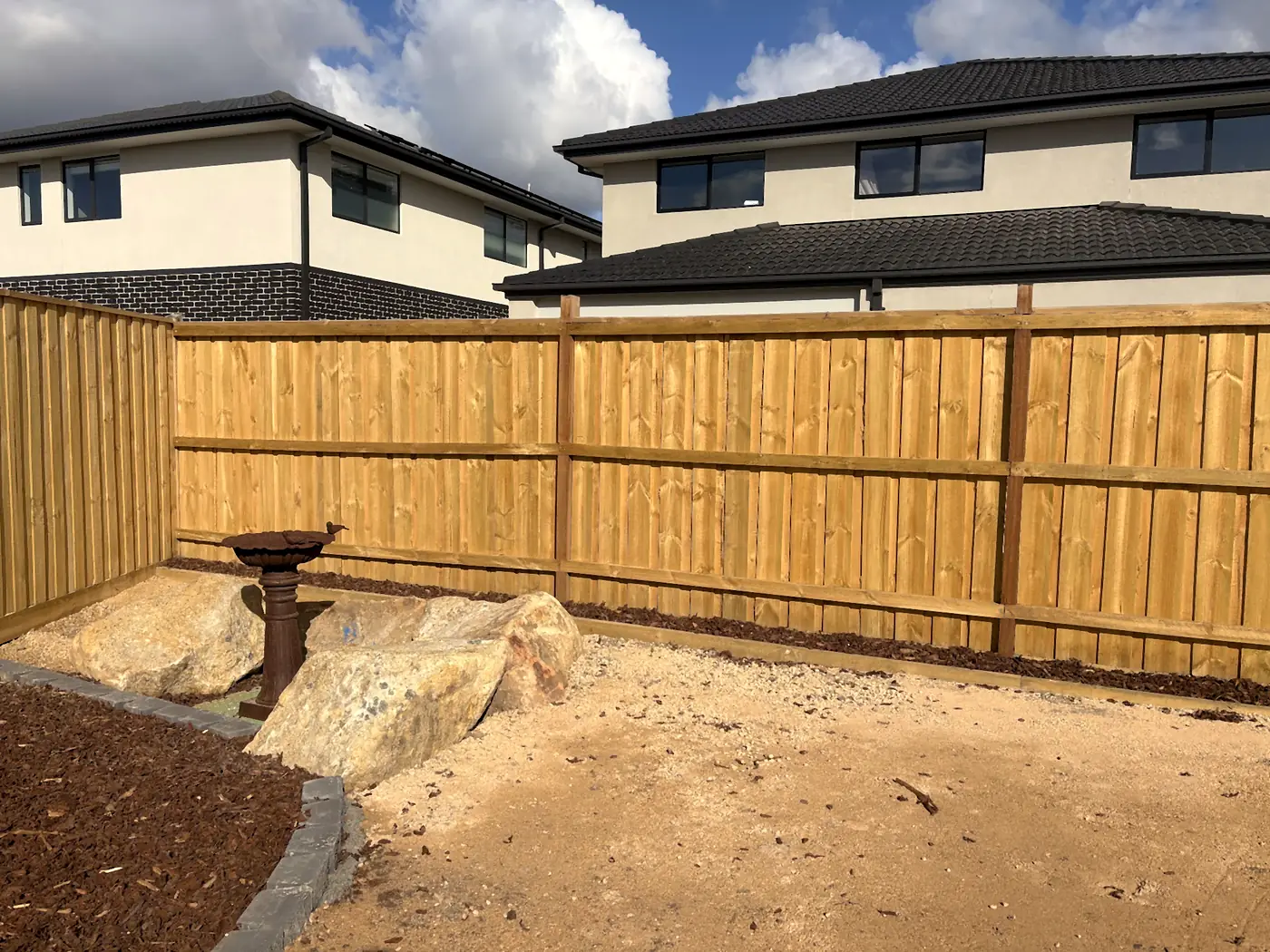 New timber paling fence with large boulders, a bird bath and new mulch