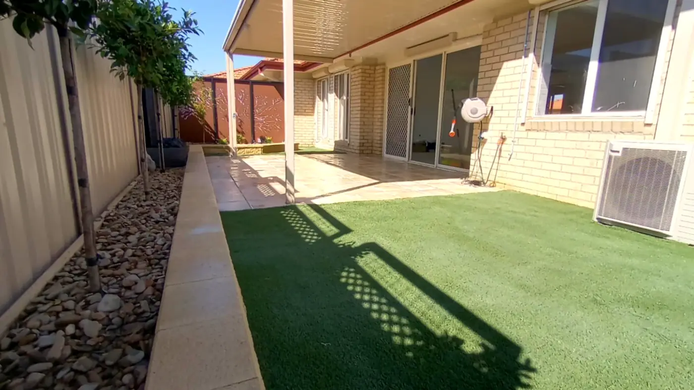 Synthetic turf with a pebble side strip and garden path along a Colorbond fence